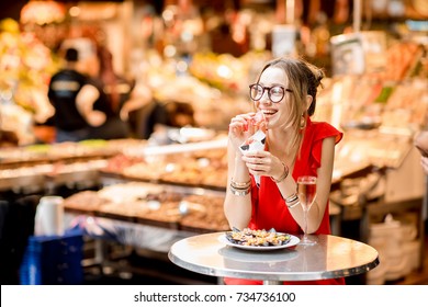 Young Woman In Red Dress Eating Jamon Traditional Spanish Dry-cured Ham Sitting At The Barcelona Food Market