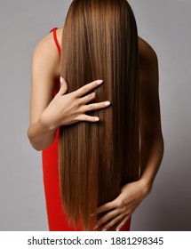 Young woman in red dress has tilted haed forward and brushes run fingers through her long silky straight hair covering face over grey wall background. Haircare beauty, wellness, hairstyle