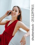 Young woman in red dress talking on phone indoors portrait