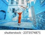 Young woman with red dress visiting the blue city Chefchaouen, Marocco - Happy tourist walking in Moroccan city street - Travel and vacation lifestyle concept