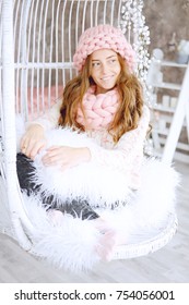 Young Woman With Red Hair And Dressed In Sweater And Knitted Pink Hat And Snood Sitting In Her Favourite Chair