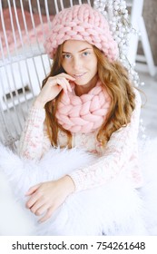 Young Woman With Red Hair And Dressed In Sweater And Knitted Pink Hat And Snood Sitting In Her Favourite Chair