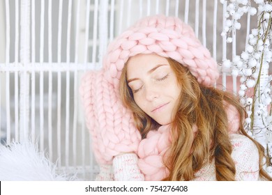 Young Woman With Red Hair And Dressed In Sweater And Knitted Pink Hat And Snood Sitting In Her Favourite Chair