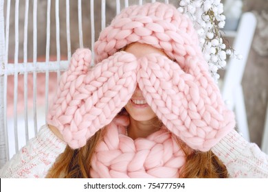 Young Woman With Red Hair And Dressed In Sweater And Knitted Pink Hat And Snood Sitting In Her Favourite Chair