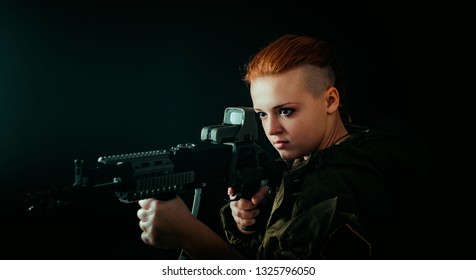 Young woman with red hair, hold machinegun and takes aim at the sight in military uniform. horizontal background