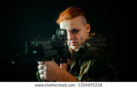 Young woman with red hair, hold machinegun in hands in military uniform. Horizontal photo