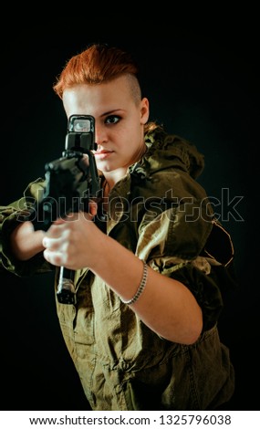 Young woman with red hair, hold machinegun in hands in military uniform. Vertical photo