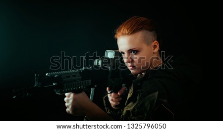 Young woman with red hair, hold machinegun and takes aim at the sight in military uniform. horizontal background