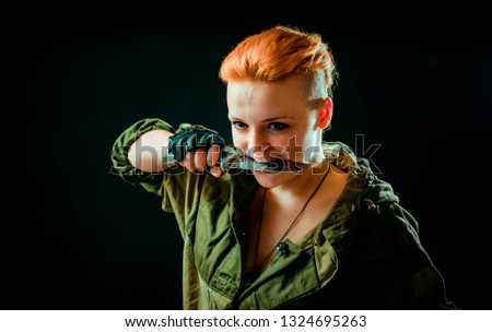 Young woman with red hair in military uniform, keep a knife in her teeth