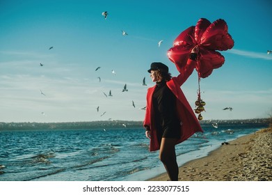 Young woman with a red heart balloons runing on the beach
