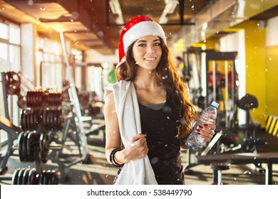 Young woman with red Santa hat, towel and water bottle in gym. Snow effect on photo.
