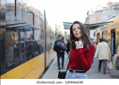 Junge Frau in rotem Hemd lächelt in einer Straßenbahnstation in der Stadt.