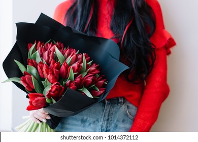 Young woman in a red sweater holding beautiful fresh blossoming red tulips flower bouquet wrapped in a black paper - Powered by Shutterstock