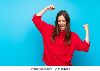 Young woman with red sweater over isolated blue background celebrating a victory