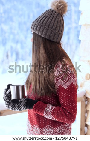 young woman in red sweater standing on a balcony with hot drink in winter