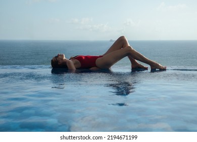 Young Woman In A Red Swimsuit Lies On The Edge Of The Pool