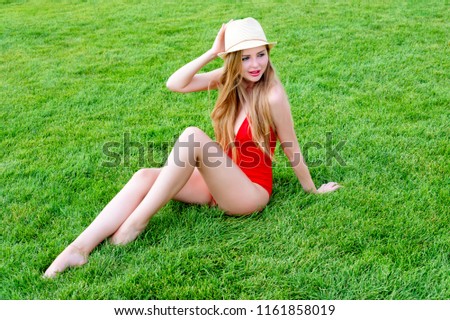 Young woman in red swimsuit sunbathing on the grass. Summer leisure, outdoors in the park at luxury resort.