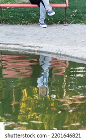 Young Woman Reflection On Water Puddle At Park