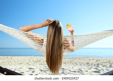 Young woman with refreshing cocktail relaxing in hammock on beach - Shutterstock ID 1909525927