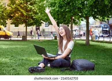 A young woman rejoices sitting on the lawn with a laptop. The girl works remotely on a laptop in the fresh air. The concept of remote work. Work in the park. - Shutterstock ID 2160162703