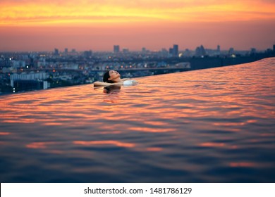 Young woman relax in swimming pool on roof top during amazing sunset and enjoy cityscape. Summer vacation and holidays concept                              