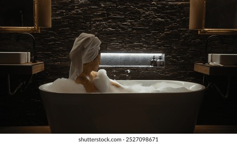 A young woman relaxes in a luxurious bathtub filled with foam, wrapped in tranquility inside a modern, stylish bathroom. - Powered by Shutterstock