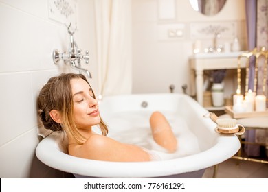 Young woman relaxing in the beautiful vintage bath full of foam in the retro bathroom decorated with candles - Shutterstock ID 776461291