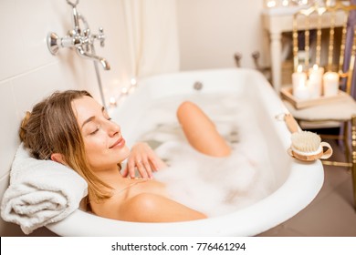 Young Woman Relaxing In The Beautiful Vintage Bath Full Of Foam In The Retro Bathroom Decorated With Candles