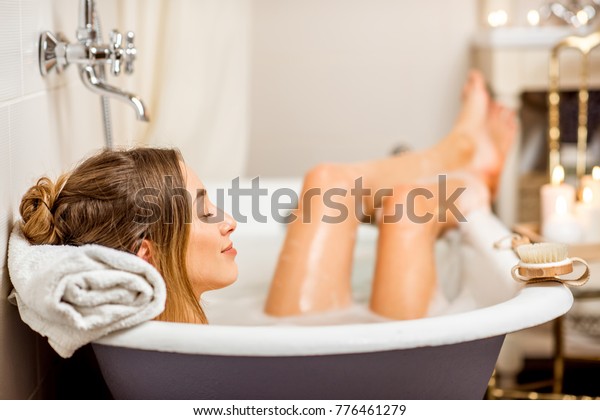 Young woman\
relaxing in the beautiful vintage bath full of foam in the retro\
bathroom decorated with\
candles