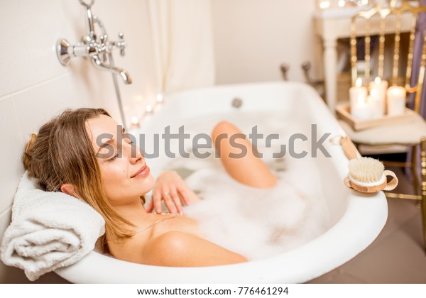 Young woman\
relaxing in the beautiful vintage bath full of foam in the retro\
bathroom decorated with\
candles