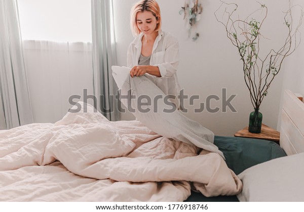 Young woman is relaxing in bed. Day off.\
Bedtime. Early morning light. White, beige, grey. Light and bright.\
Morning ritual. Apartment lifestyle living. Cozy bed linen. Soft\
pillow and\
comforter.Focus