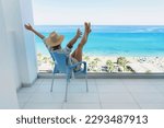 Young woman relaxing in chair on balcony of beachfront hotel or apartment.