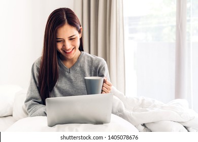 Young woman relaxing and drinking cup of hot coffee or tea using laptop computer on a cold winter day in the bedroom.woman checking social apps and working.Communication and technology concept