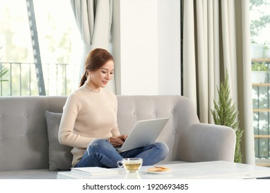 Young woman relaxing and drinking cup of hot coffee or tea using laptop computer