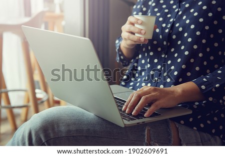 Young woman relaxing and drinking cup of hot coffee or tea using laptop computer in the cafe. Cozy office workplace, remote work,