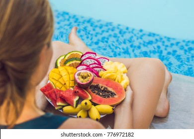 Young Woman Relaxing And Eating Fruit Plate By The Hotel Pool. Exotic Summer Diet. Photo Of Legs With Healthy Food By The Poolside, Top View From Above. Tropical Beach Lifestyle.