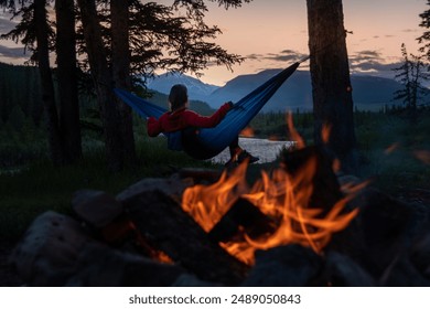 A young woman relaxing in a hammock near a campfire, looking at the Red Deer River at the Eagle Creek Campground in Yaha Tinda, Alberta, Canada. - Powered by Shutterstock