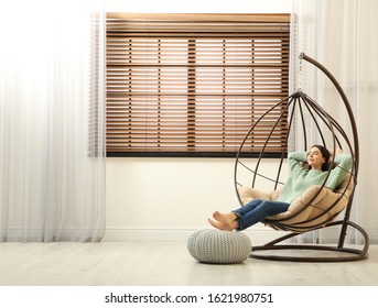 Young woman relaxing in hanging chair near window at home. Space for text - Powered by Shutterstock