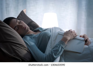 Young woman relaxing in her bed at night, she is falling asleep while reading a book - Shutterstock ID 1304633590
