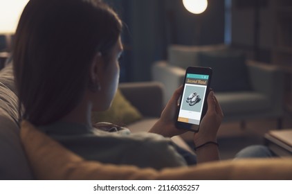 Young Woman Relaxing At Home And Connecting With Her Smartphone, She Is Searching Second Hand Items On A Shopping App