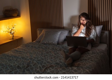 Young Woman Relaxing At Home Late At Night, Sitting In Bed With Laptop Computer In Her Lap, Shopping Online