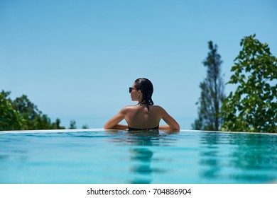 Young Woman Relaxing In Infinity Swimming Pool Looking At View