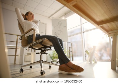 Young Woman Relaxing In Office Chair At Workplace, Low Angle View