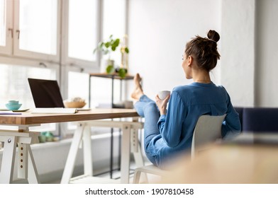 Young Woman Relaxing In Office With Her Bare Feet On Desk 
