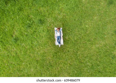 Young Woman Relaxing On A Rug On The Grass Viewed From High Overhead As A Diminutive Person In The Center Of A Field Of Green Grass