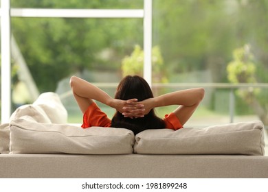 Young woman relaxing on sofa at home, back view