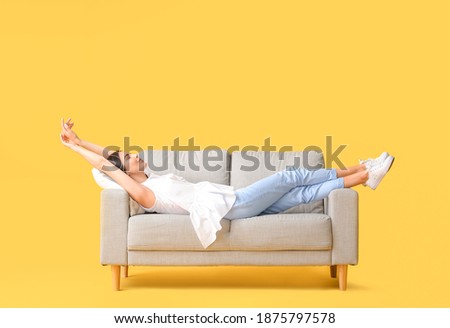 Young woman relaxing on sofa against color background