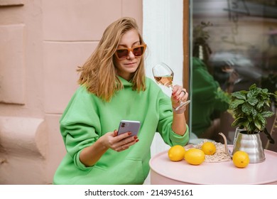 Young Woman Relaxing On Summer Terrace Drinking Wine And Using Mobile Phone.