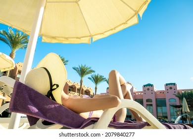 Young woman relaxing outdoors on sunny summer day. Happy lady lying down on comfortable beach chair sunbathing. Calm girl in straw hat enjoying fresh air relaxing.