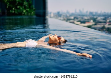 Young woman relaxing in roof top swimming pool and floating in water. Summer vacation concept